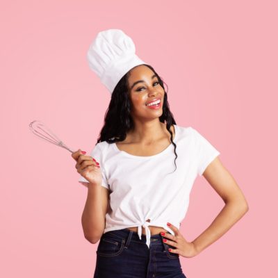 Portrait of a smiling young female chef with whisker looking at camera, against pink studio background